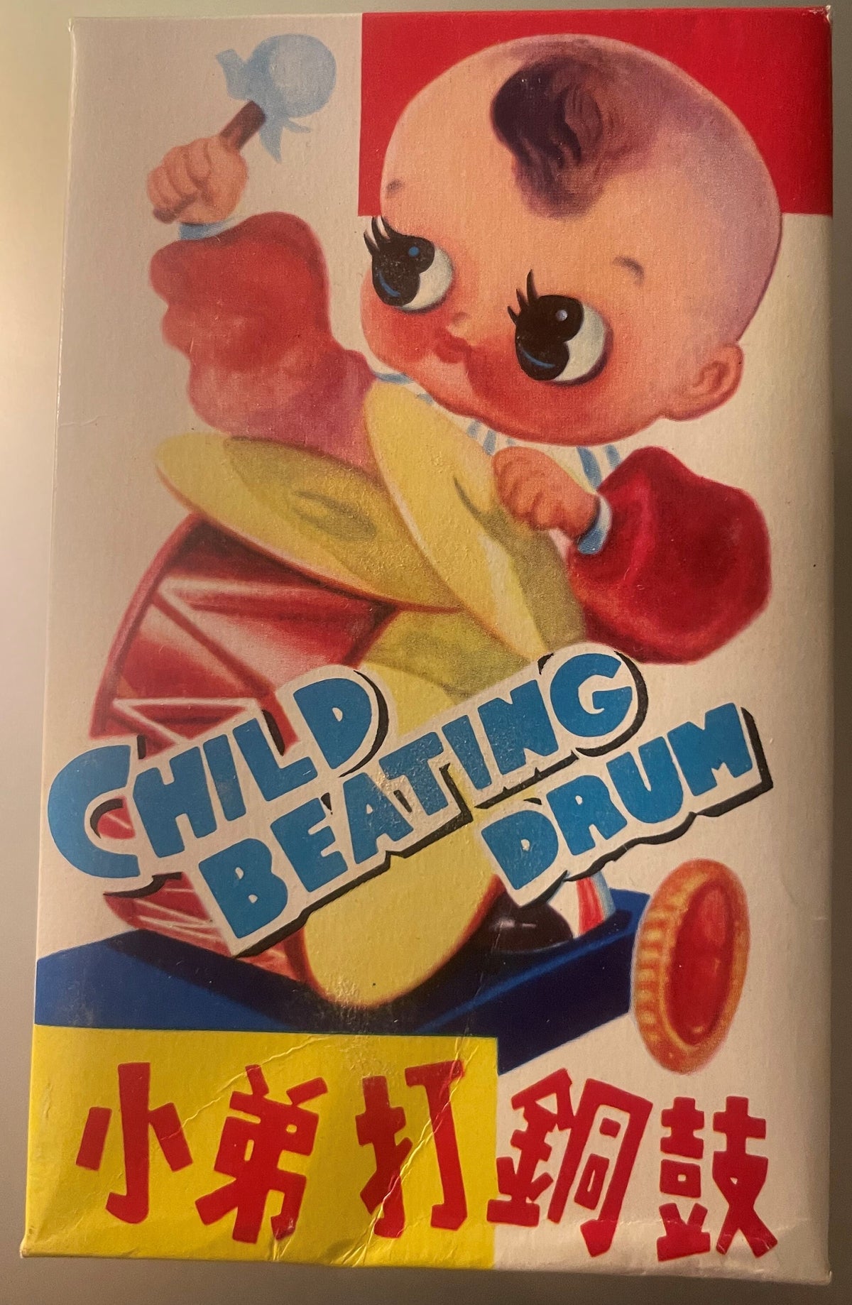 Vintage toy box front showing smiling baby face in red and yellow clothing holding drum, with "Child Beating Drum" text and C