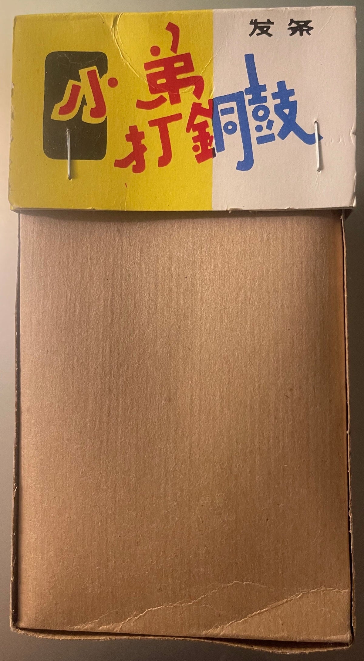 Vintage tin toy box with yellow and white panels, red and blue Chinese characters, and dark rectangular illustration on left 