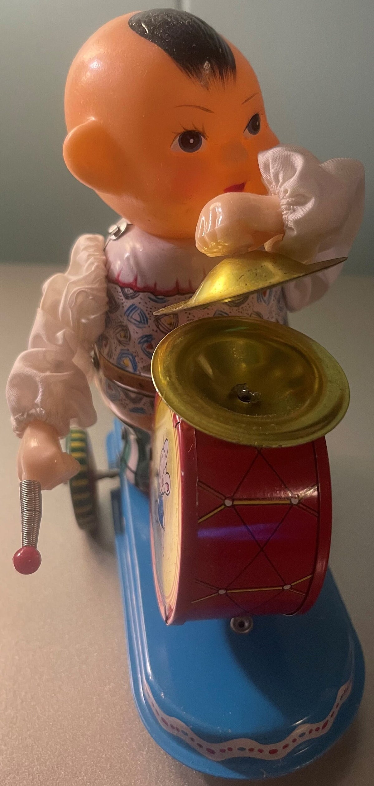 Vintage tin clockwork drummer toy with orange head, white ruffled collar, red drum with gold cymbal, blue base, shown