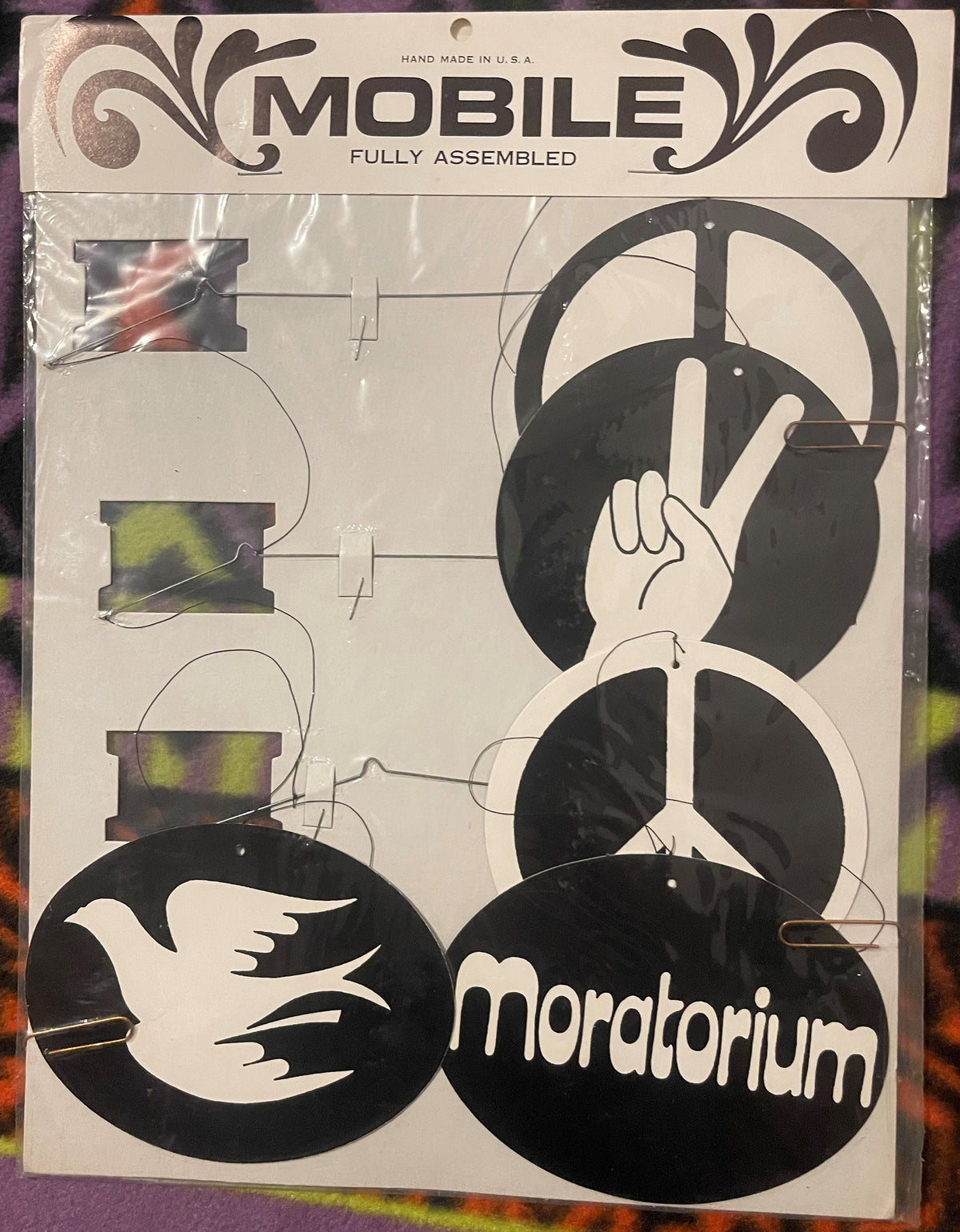 Sealed package of a black and white peace mobile with dove, peace hand gesture, and circular ornaments, marked "Moratorium"