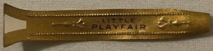 Gold foil embossed cigar band with "Playfair" text, displayed flat against tan fabric for scale