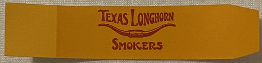 Vintage Texas Longhorn Smokers cigar band with gold background and burgundy text, displayed flat on textured fabric.