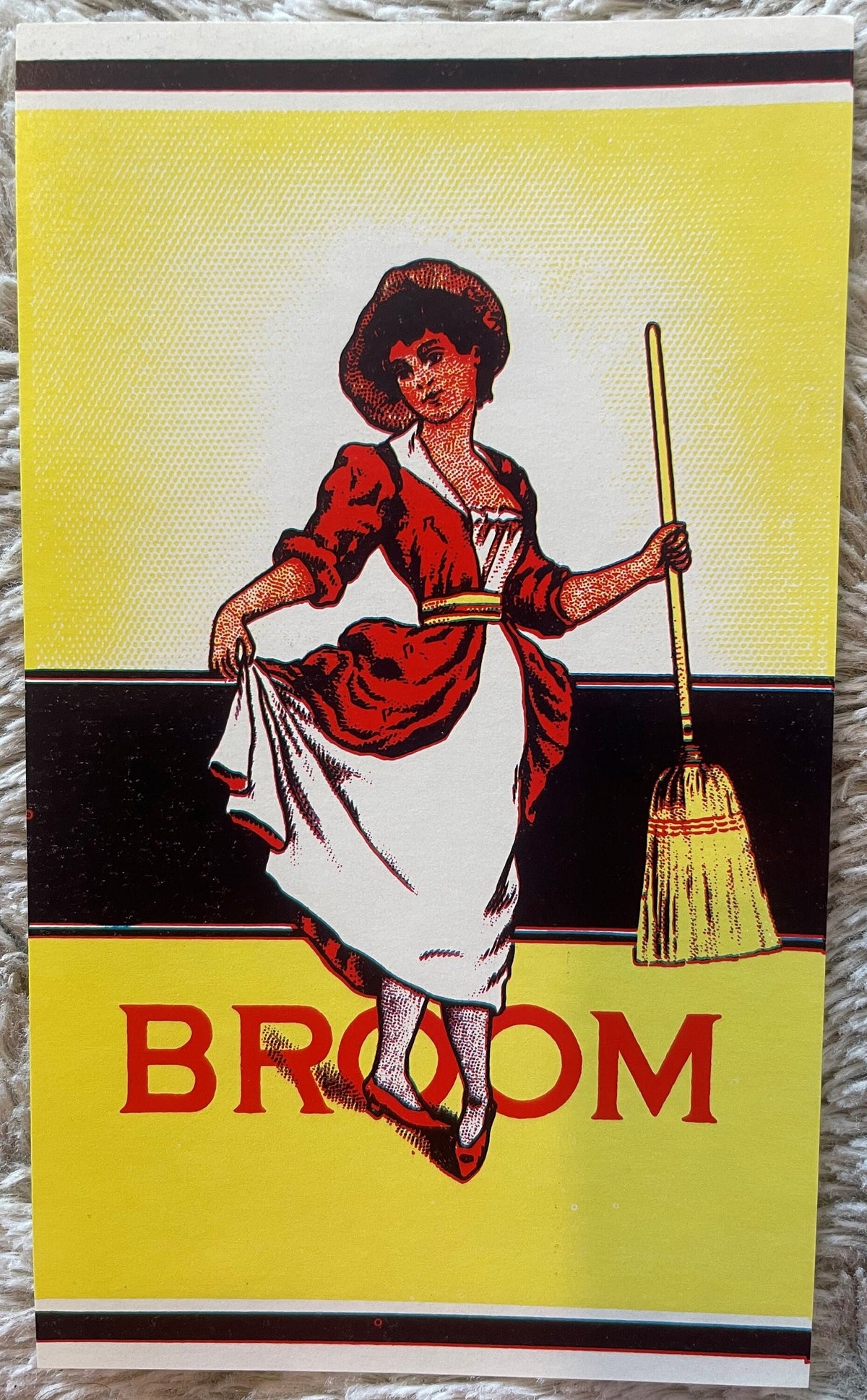 Antique broom label featuring a dancing woman in red dress holding a yellow broom against yellow and black striped background