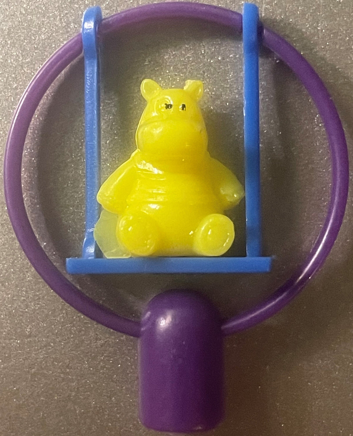 A yellow hippo pencil topper on a blue swing inside a purple frame