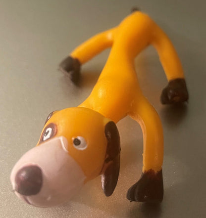 Vintage bendable poseable dog toy with orange body, white snout, and dark brown ears and paws, posed in stretching position on gray surface.