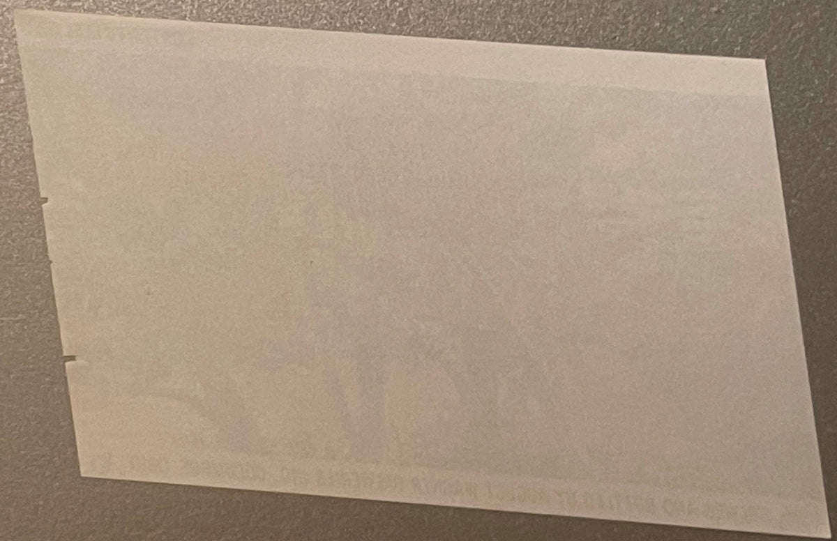 Blank cream-colored vintage beer label on gray textured surface, shown at an angle with visible binding holes on left edge