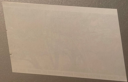 Blank cream-colored vintage beer label on gray textured surface, shown at an angle with visible binding holes on left edge