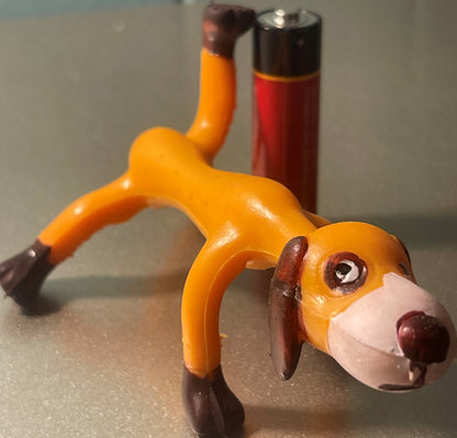 Vintage orange and brown bendable dog toy with articulated limbs in play position, photographed alongside a red condiment bottle for scale.