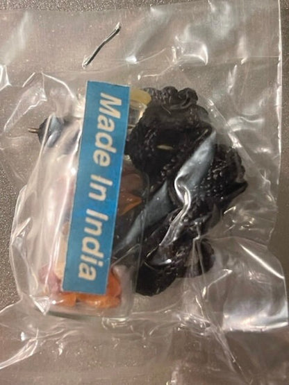 Sealed plastic bag containing dark black gemstone chips in a glass vial with "Made in India" label, viewed from above