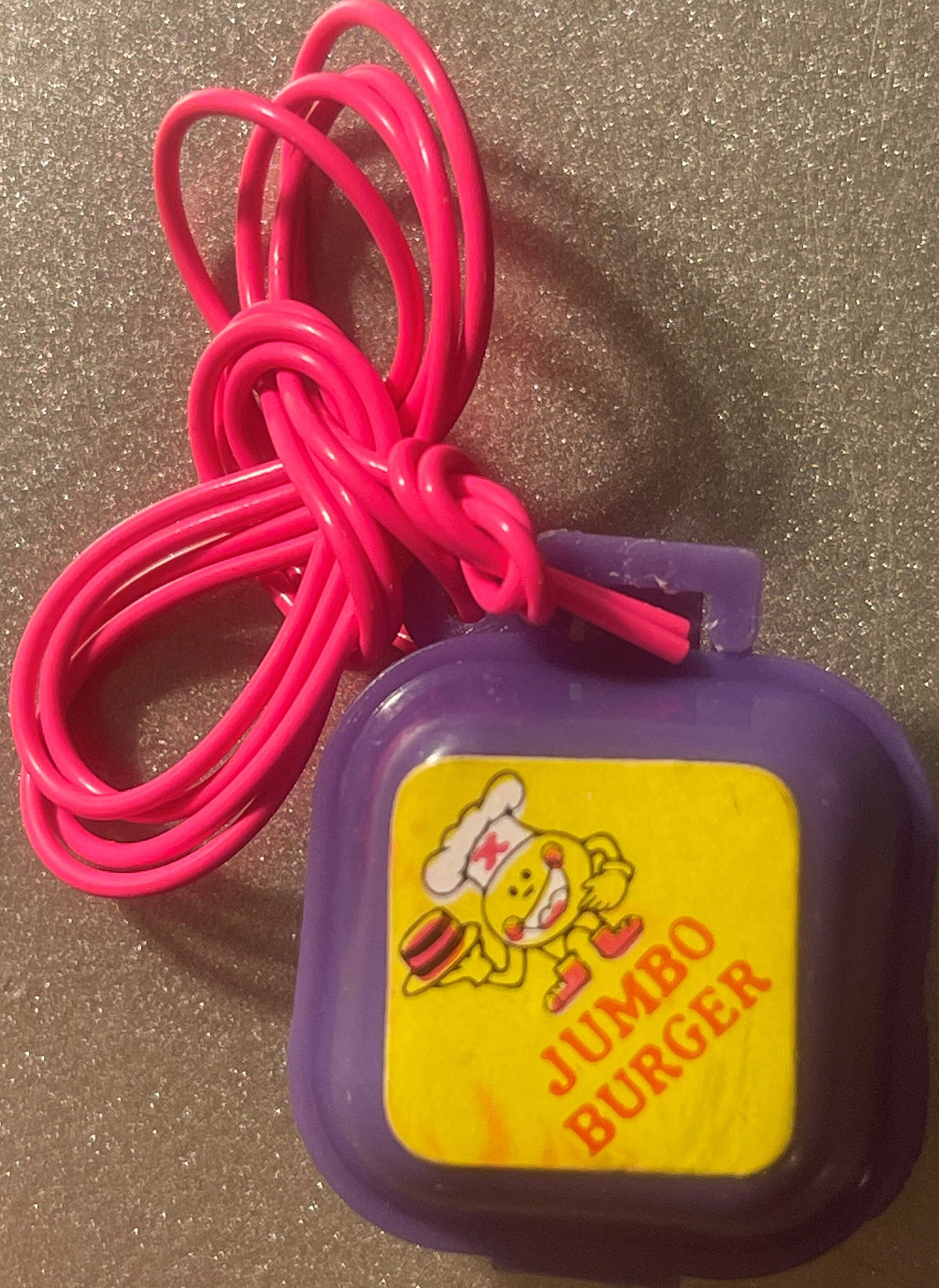 Purple Jumbo Burger charm box on a hot pink cord, yellow label with a running cartoon chef holding a hamburger and JUMBO BURGER lettering