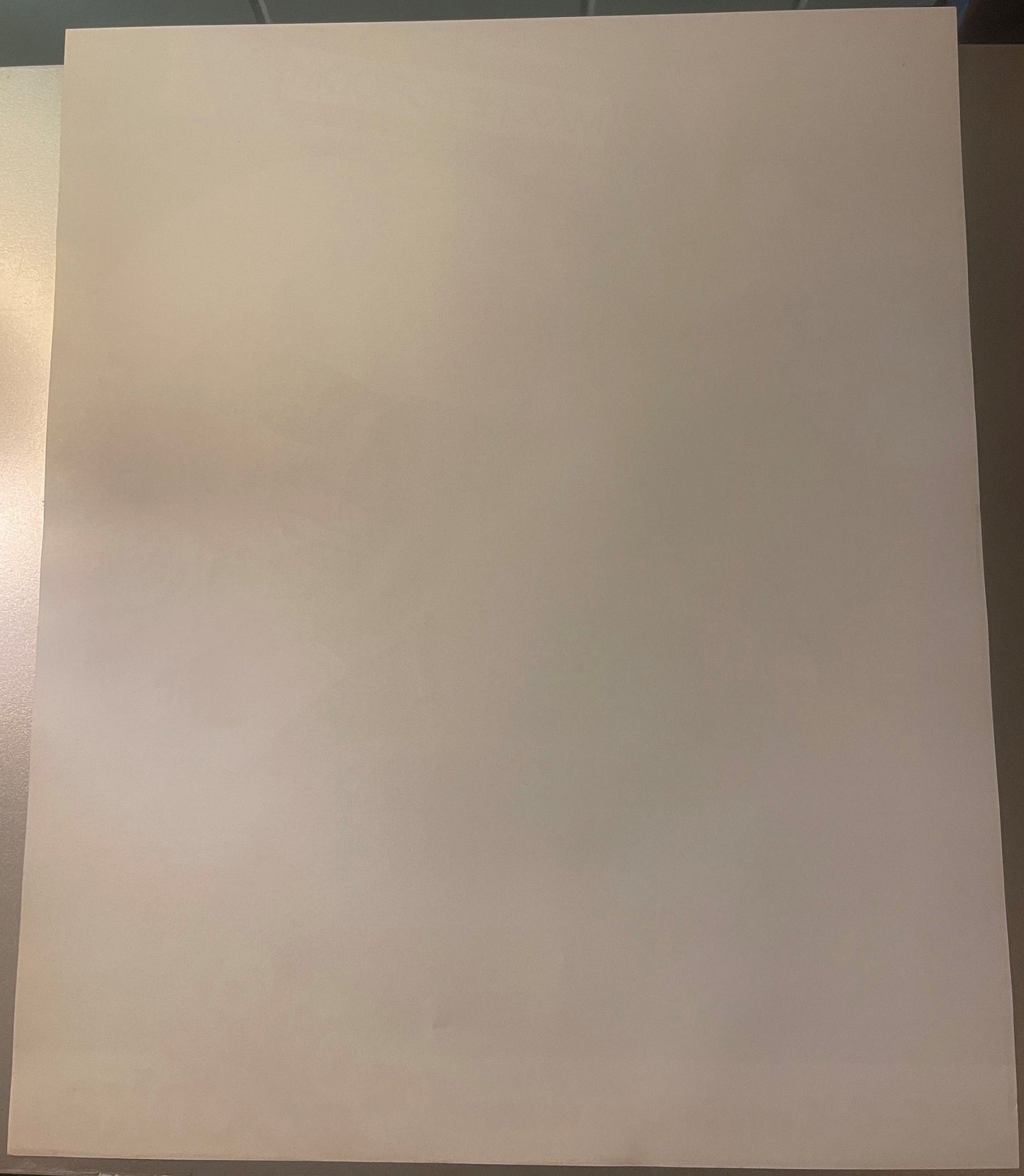 Blank cream-colored poster page photographed flat against gray tile background with natural lighting from left side