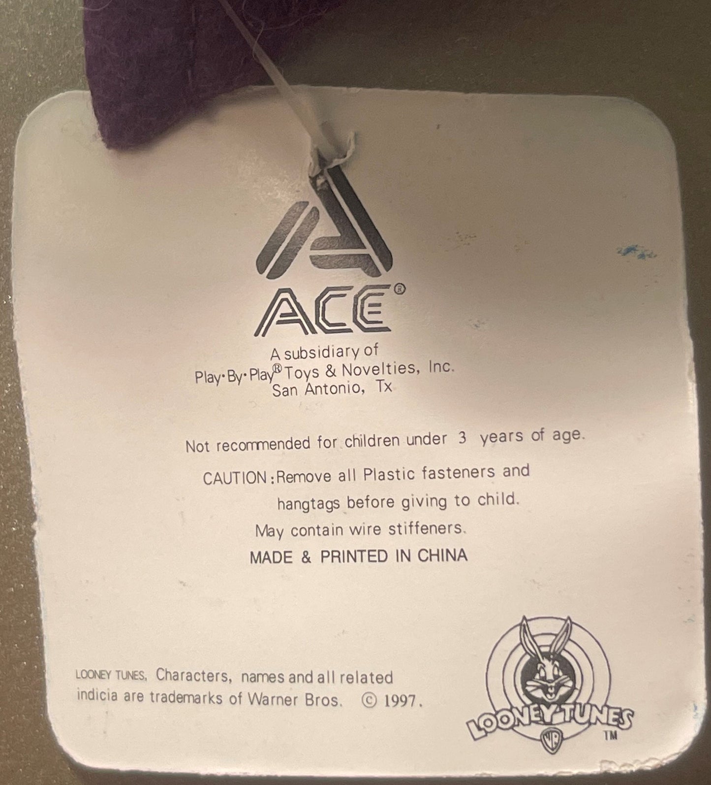 Close-up of product tag showing ACE Toys logo, Warner Bros. Looney Tunes copyright 1997, and safety warnings printed in black