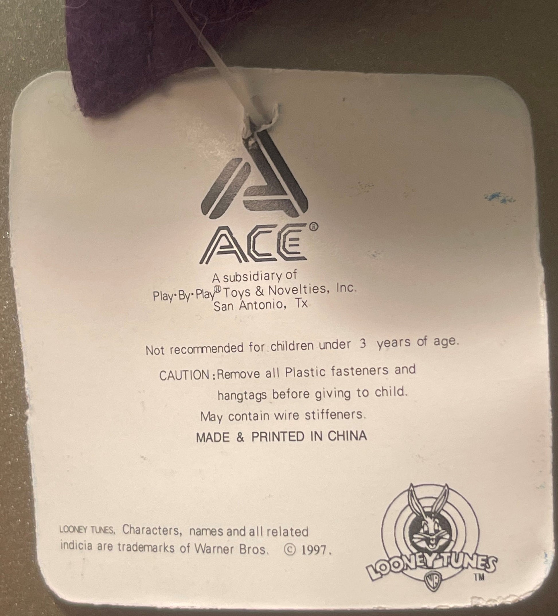 Close-up of product tag showing ACE Toys logo, Warner Bros. Looney Tunes copyright 1997, and safety warnings printed in black