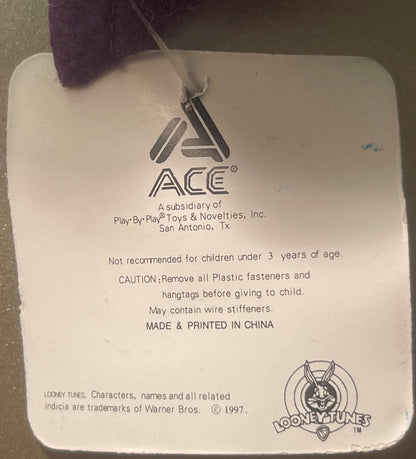 Close-up of product tag showing ACE Toys logo, Warner Bros. Looney Tunes copyright 1997, and safety warnings printed in black