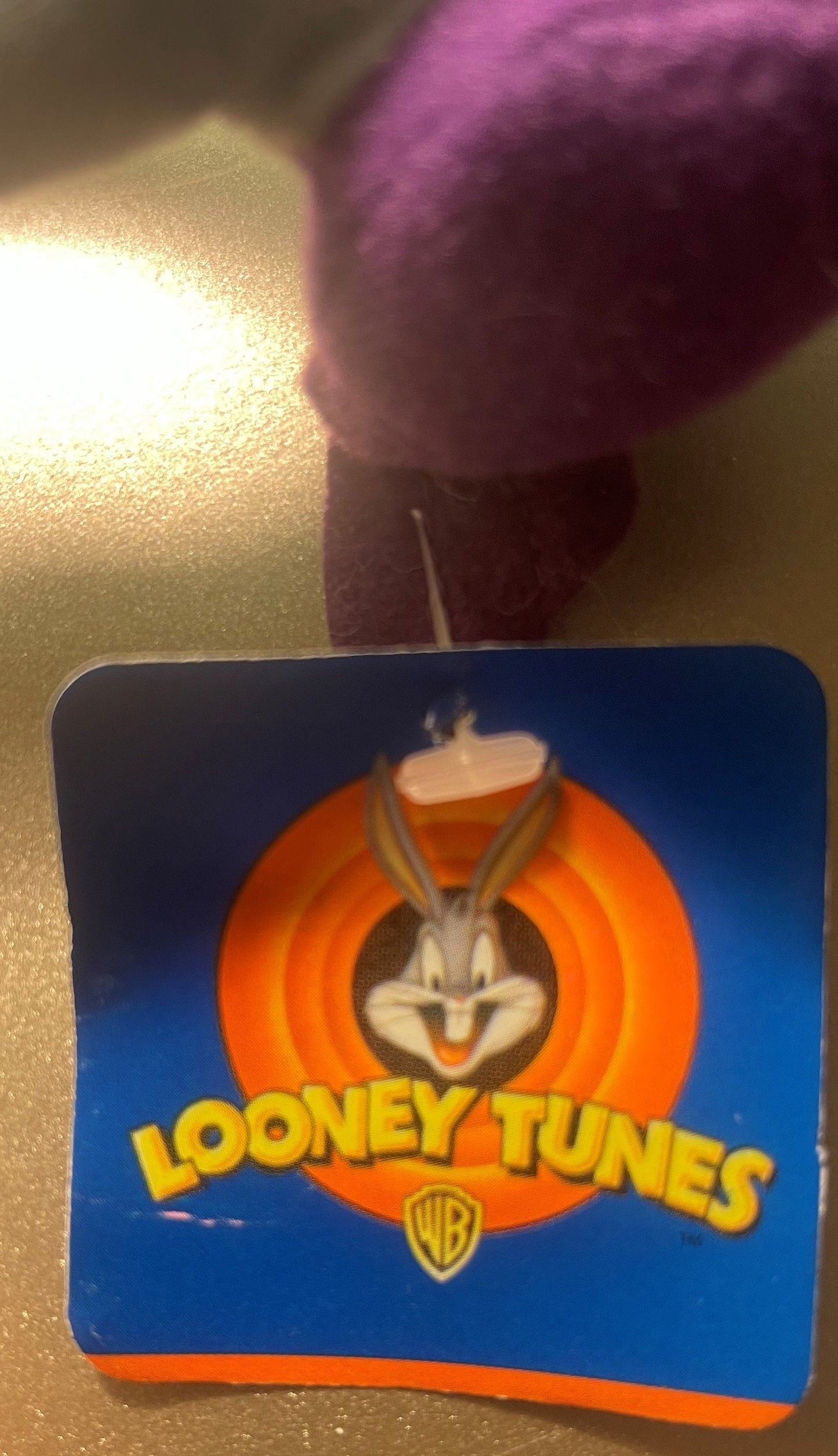 Looney Tunes coaster with Bugs Bunny logo held up against textured wall surface, showing blue background and orange circular 