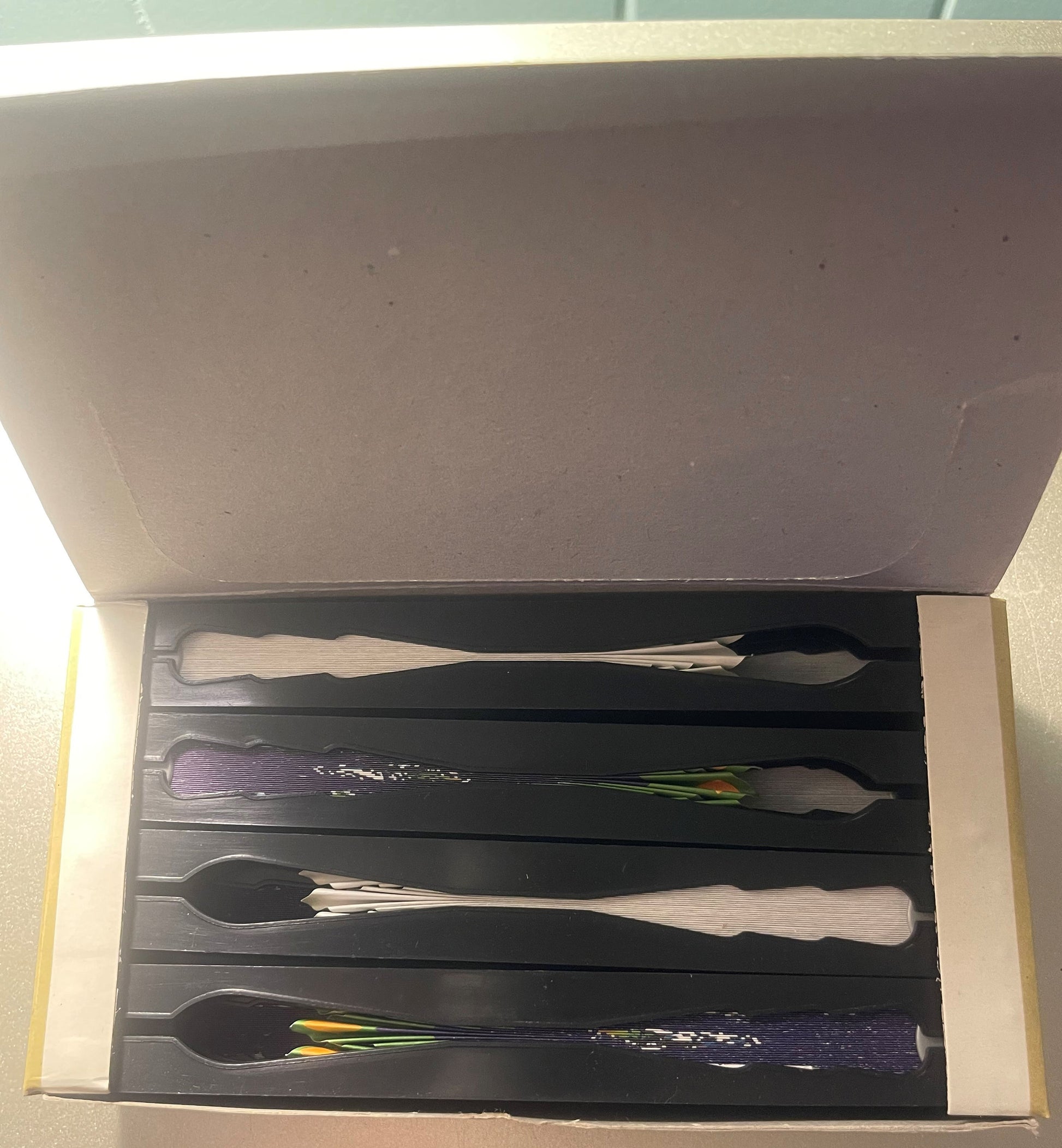 Unboxed set of four decorative spoons with handles featuring purple flowers, white handles, and black handles in a black disp
