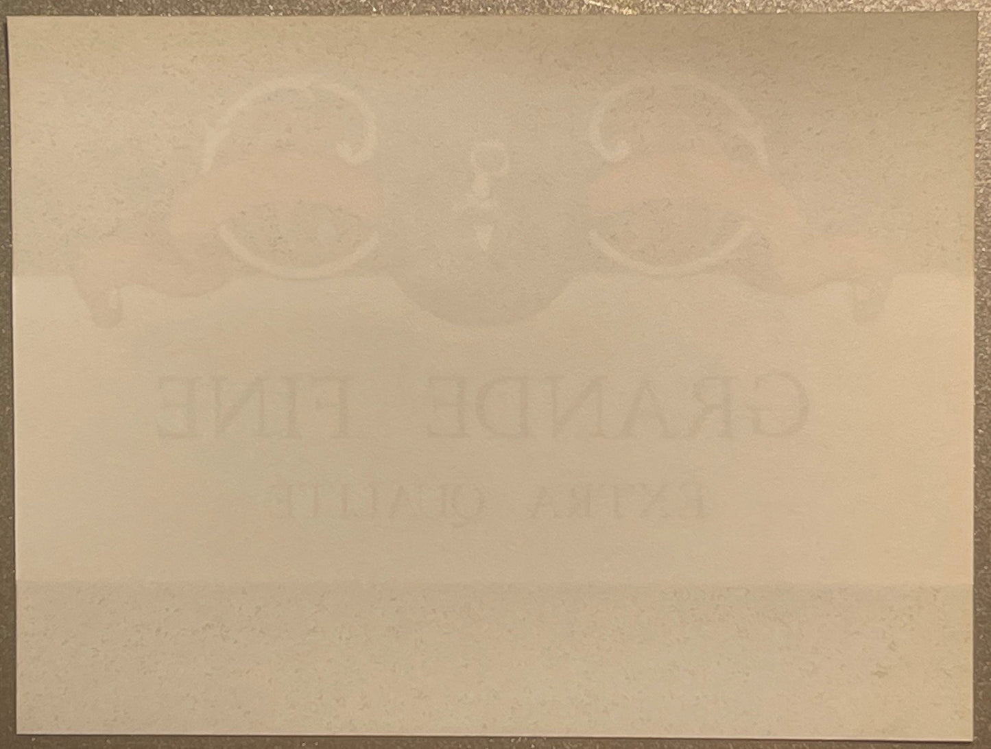 Faded cream-colored vintage wine label with embossed circular designs at top and partially visible text, photographed flat ag