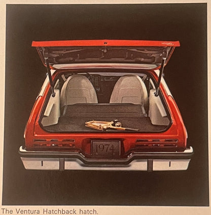 Rear view of a red and white 1974 Pontiac Ventura with open hatchback showing interior seats and cargo area against brown