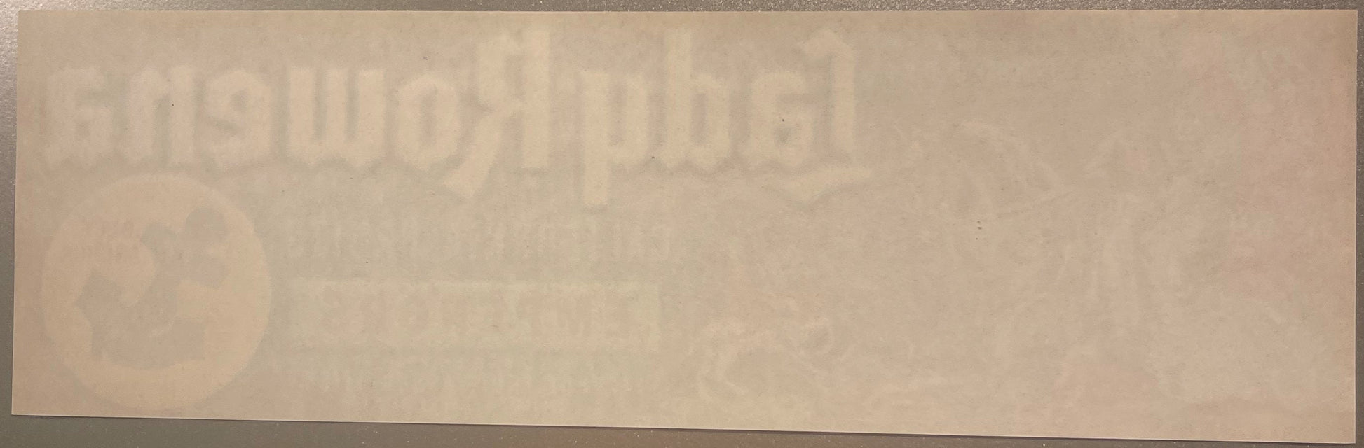Faded vintage crate label with embossed text and circular design, cream-colored paper with age spots and wear
