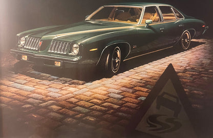 Dark green Pontiac sedan with gold interior visible through windows, parked on brick pavement at night with dramatic lighting