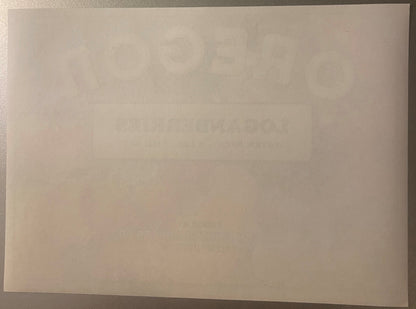Oregon Loganberries crate label, reverse: the blank back of the label in cream stock on a gray surface, with the OREGON and LOGANBERRIES lettering from the front showing through the paper in mirror image