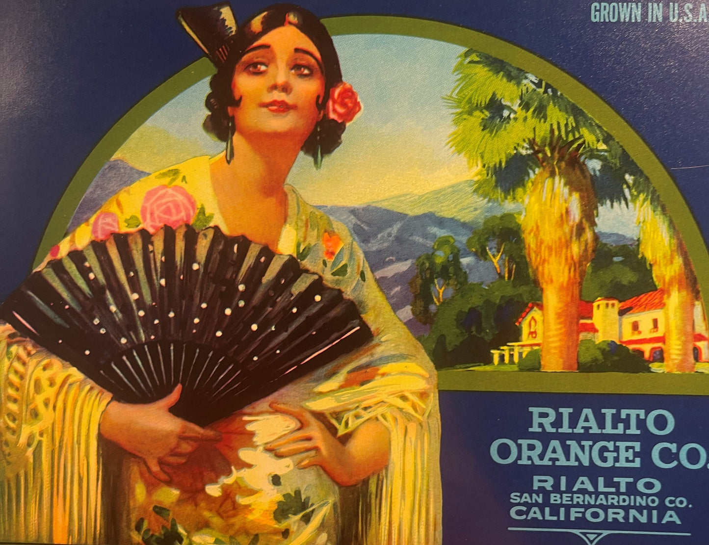 Vintage fruit crate label featuring a Spanish woman in yellow dress holding a black fan, with mission architecture and palm t
