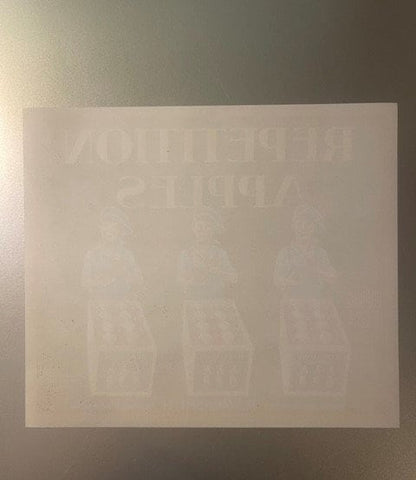 Faded cream-colored vintage apple crate label with embossed text and repeated imagery, photographed flat against gray backgro