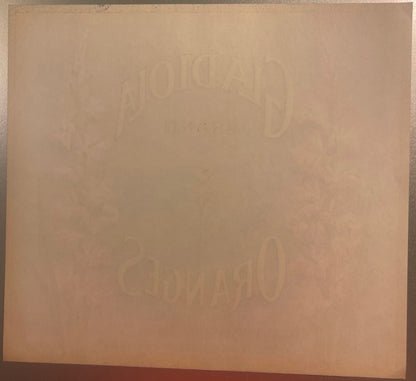 Faded embossed fruit crate label with "Gladiola" and "Covina" text visible on aged tan cardboard, photographed flat against d