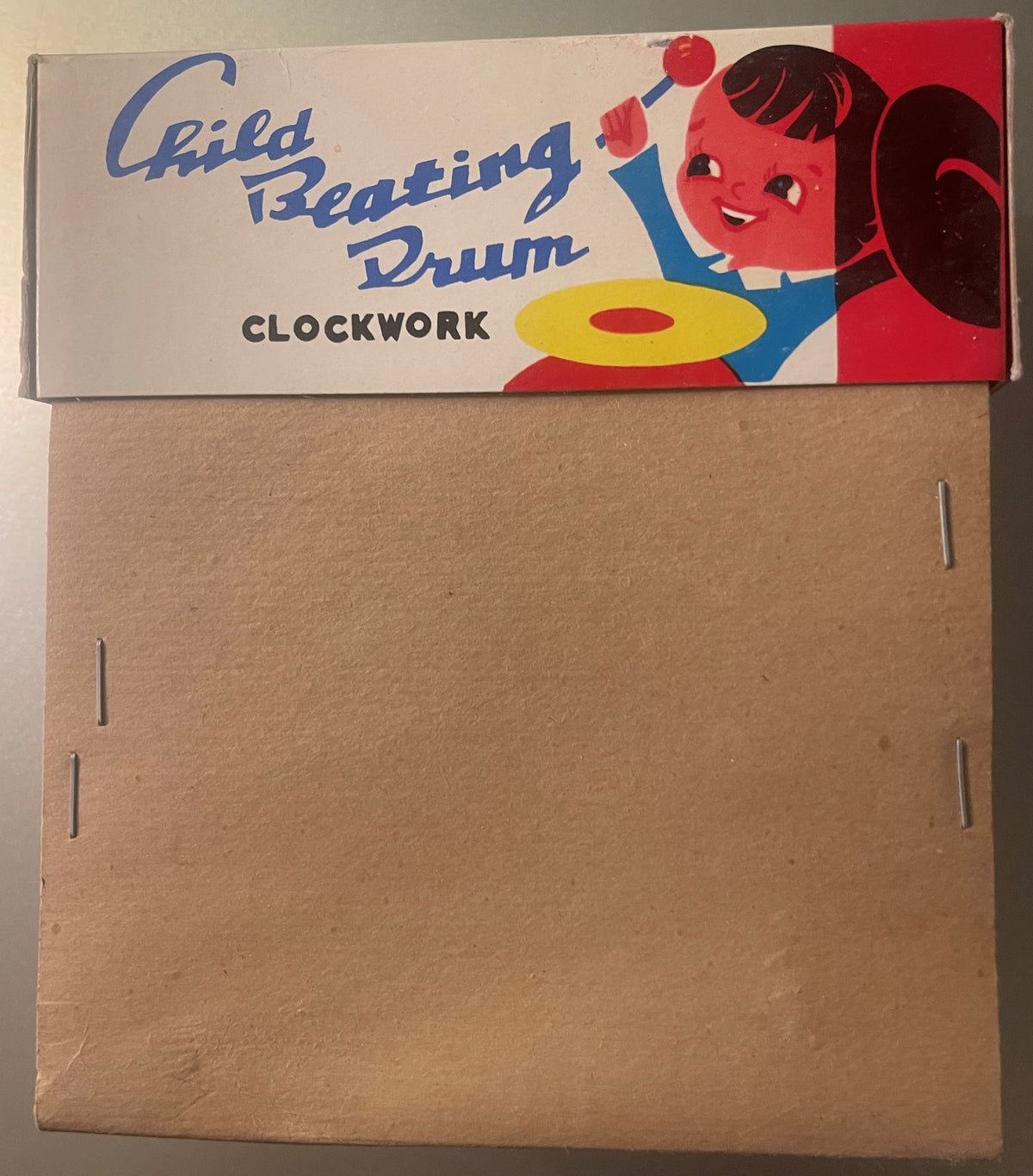 Vintage clockwork tin boy drummer toy in original box showing red smiling face, blue arms, yellow drum, displayed against tan