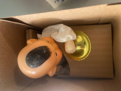Orange tin wind-up drummer toy with a white cloth hat, in its cardboard box, viewed from above