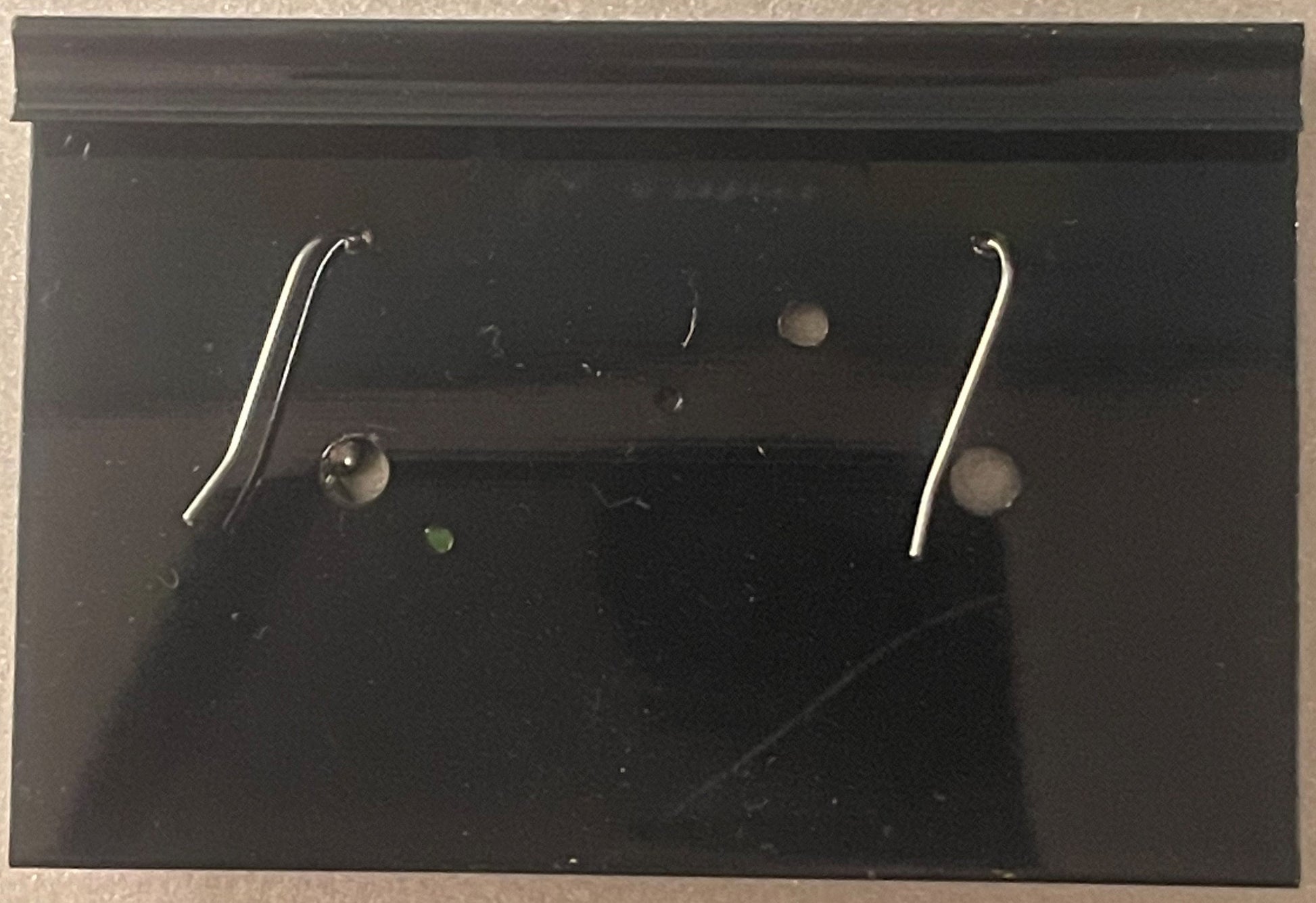 Pair of silver curved hook earrings displayed on black card backing with small round fasteners visible