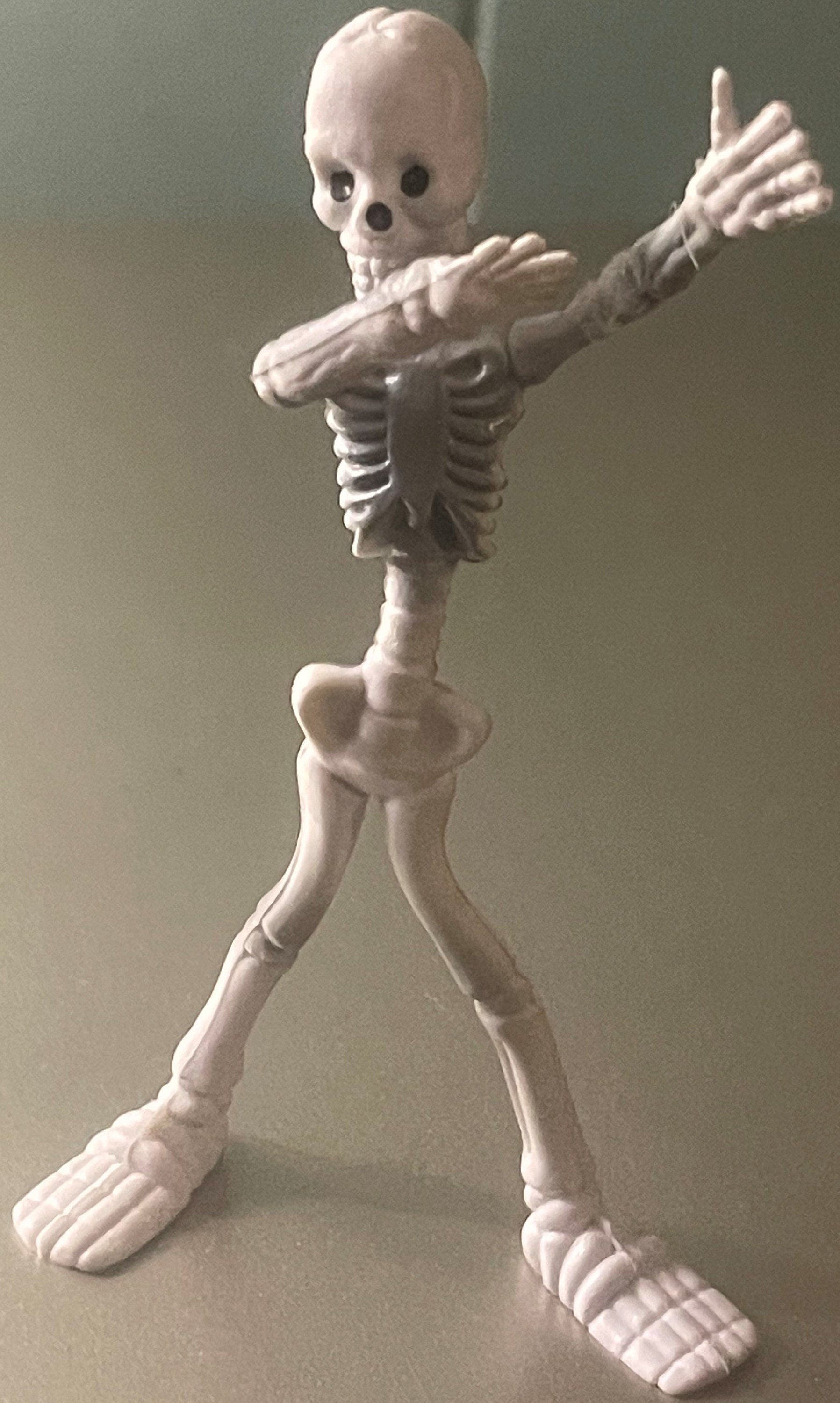 Vintage white plastic skeleton figure in dynamic pose with one arm raised, detailed ribcage and joints visible, standing agai
