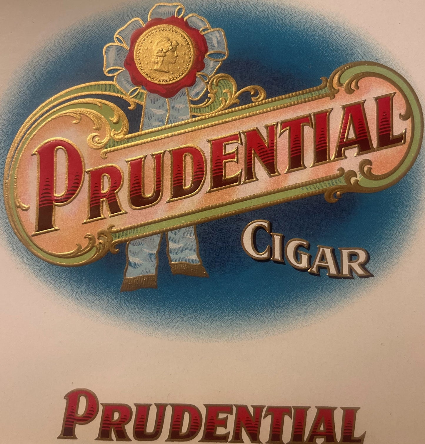 Vintage Prudential cigar label with embossed red and gold lettering, decorative scrollwork, and a medal medallion at top agai