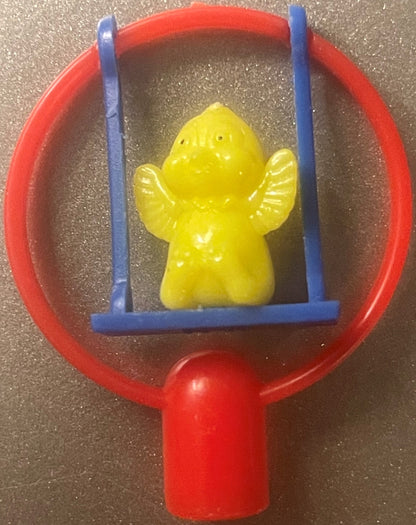 A yellow winged figure pencil topper on a blue swing inside a red frame