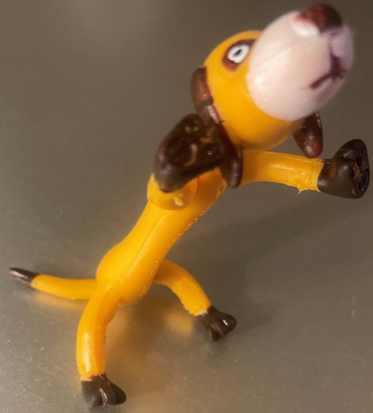 Vintage bendable poseable dog toy figure with yellow body, brown limbs and head, white face with painted features, and yellow collar, photographed from front angle against neutral background.
