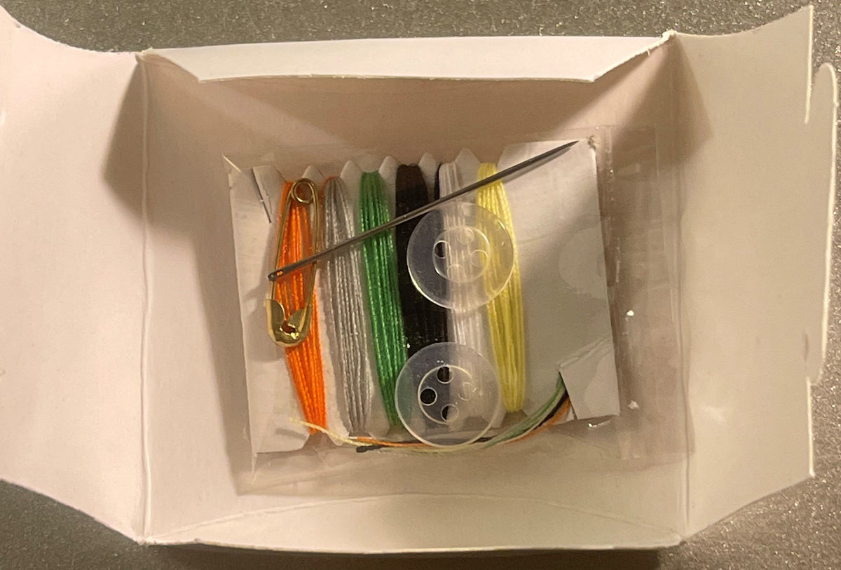 Opened white box containing colorful thread spools in orange, silver, green, black, and yellow with two clear bobbins and a n