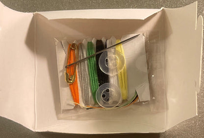 Opened white box containing colorful thread spools in orange, silver, green, black, and yellow with two clear bobbins and a n