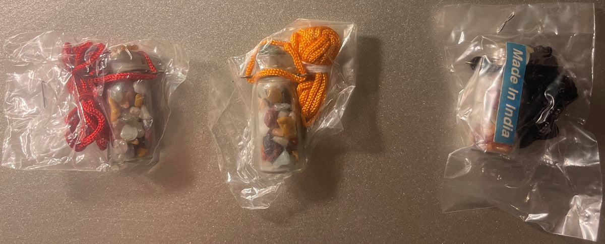 Three sealed plastic bags containing glass vials with colorful fabric wraps (red, orange, black) and gemstone chips inside, o