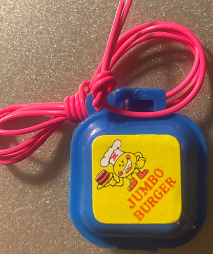 Blue Jumbo Burger charm box with hot pink cord knotted through its loop, yellow label with cartoon chef and orange-red JUMBO BURGER lettering