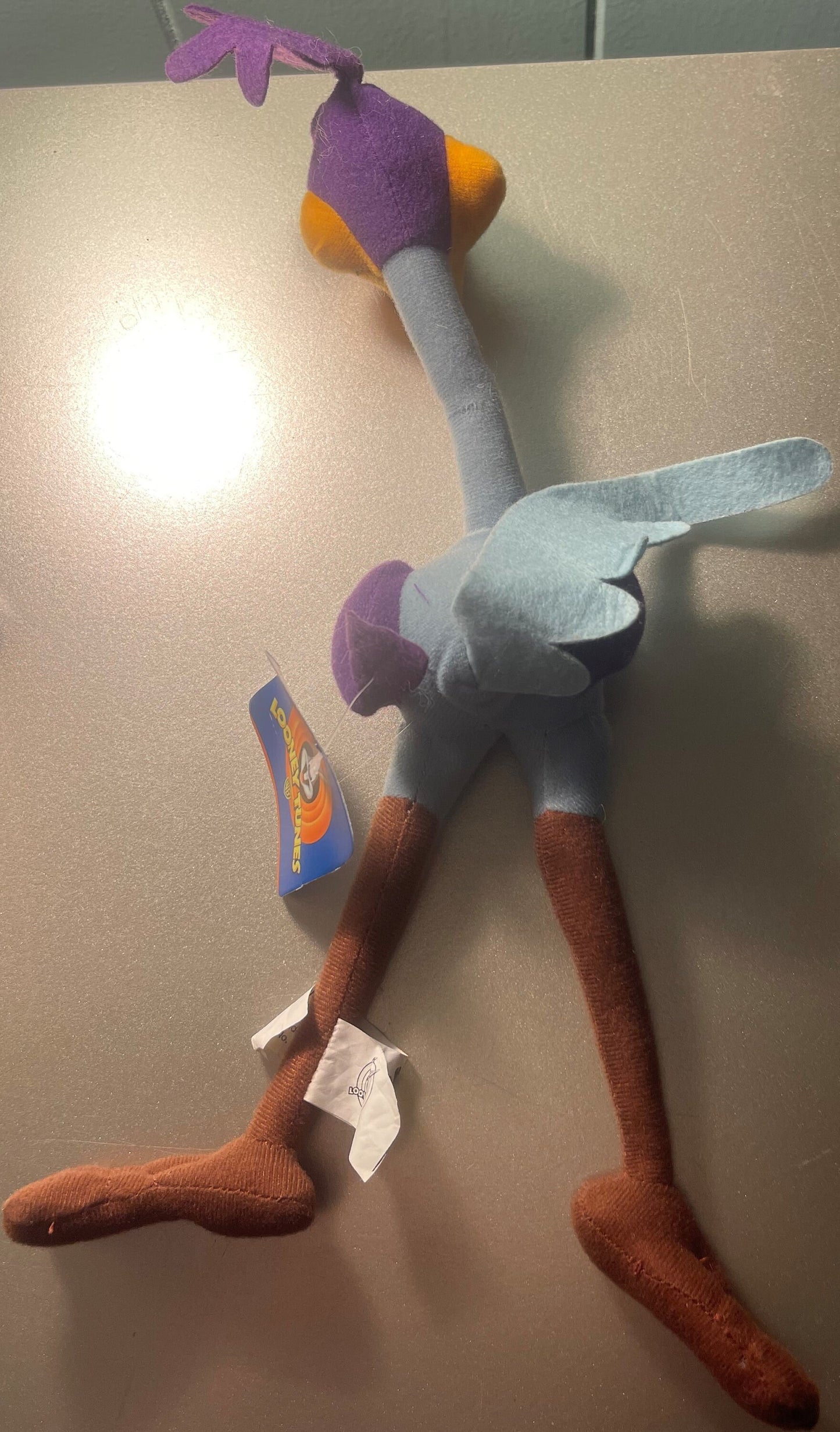 Vintage Road Runner plush toy displayed on tan surface, showing purple head with orange beak, gray body, white wings, and bro