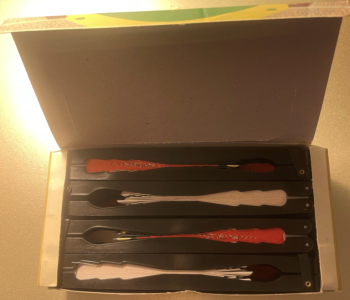 Open box containing four decorative folding fans with wooden handles in red, natural wood, and dark finishes, arranged in black compartments; vintage Baltimore Orioles merchandise.