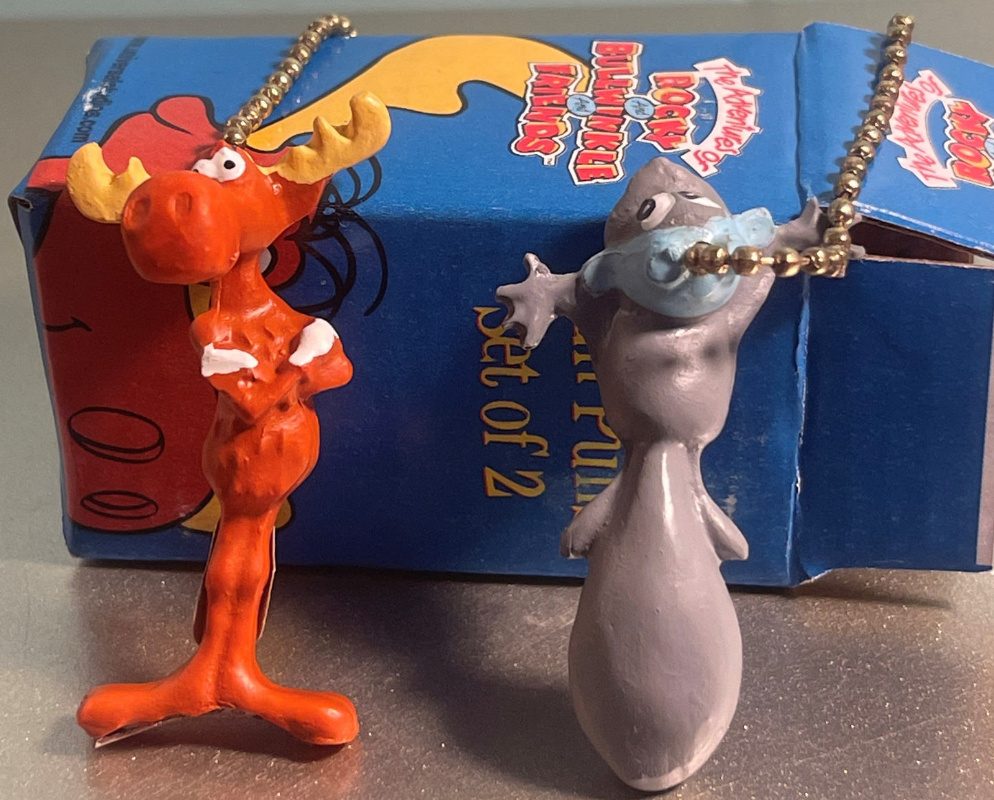Two plastic ceiling fan pull chains displayed in front of blue Rocky and Bullwinkle box: orange squirrel figure with gold cha