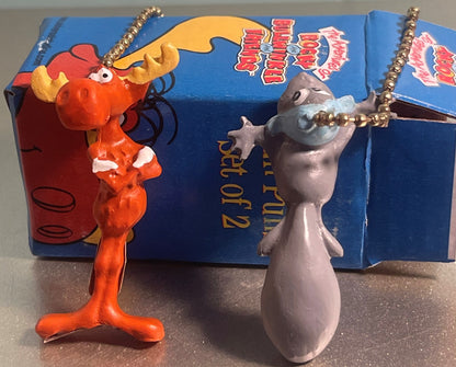 Two plastic ceiling fan pull chains displayed in front of blue Rocky and Bullwinkle box: orange squirrel figure with gold cha