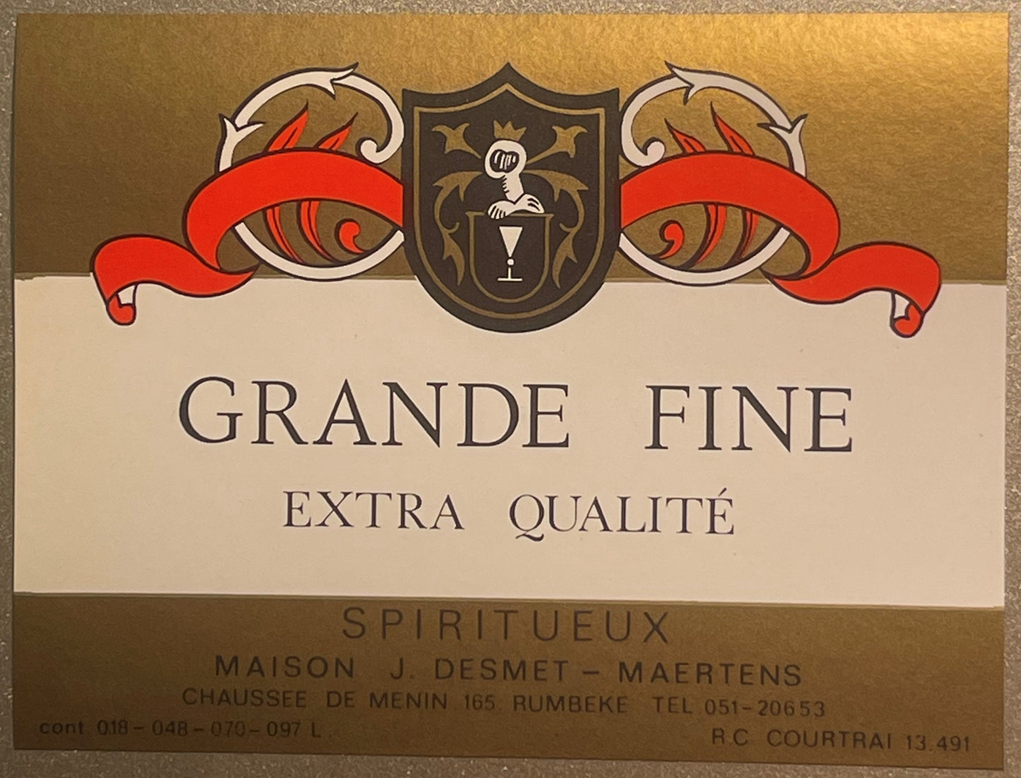 Vintage wine label with ornate red ribbons and shield crest, reading "Grande Fine Extra Qualité Spiritueux" from J. Desmet-Ma