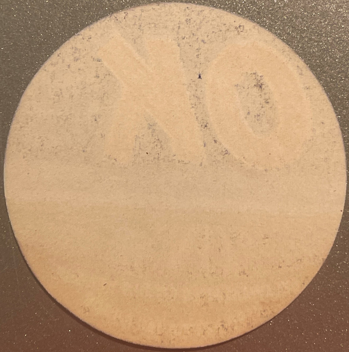 Circular tan citrus crate label with small dark specks, photographed flat against dark background, showing weathered surface 