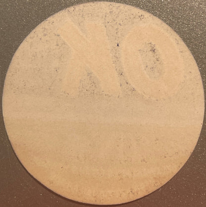 Circular tan citrus crate label with small dark specks, photographed flat against dark background, showing weathered surface 
