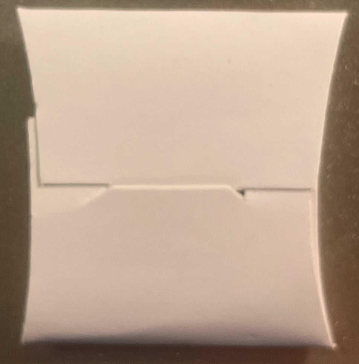 White unopened rectangular box with horizontal seam line across center, photographed straight-on against neutral background