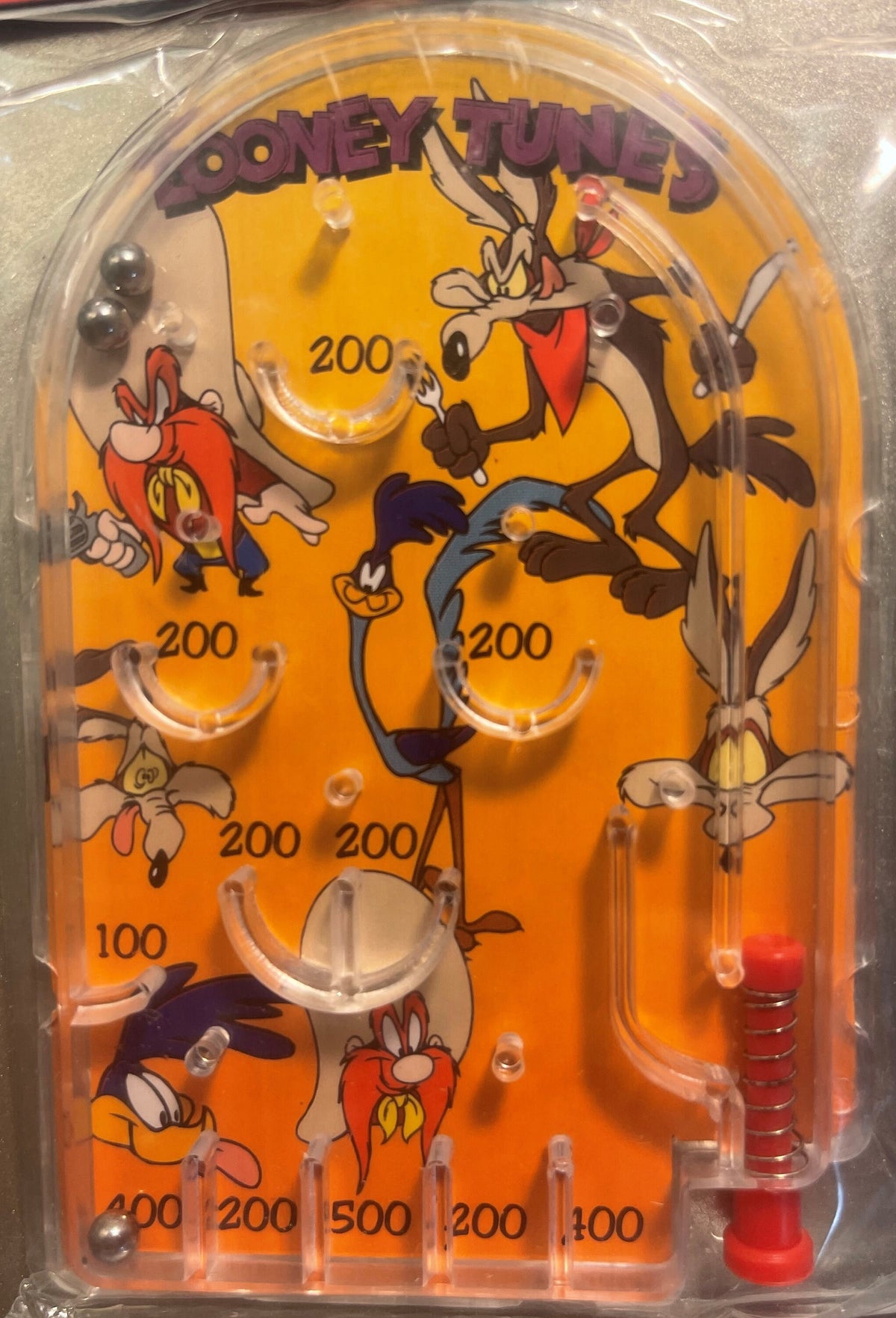 Vintage Looney Tunes mini pinball game with orange playfield featuring Wile E. Coyote and other characters, numbered scoring 