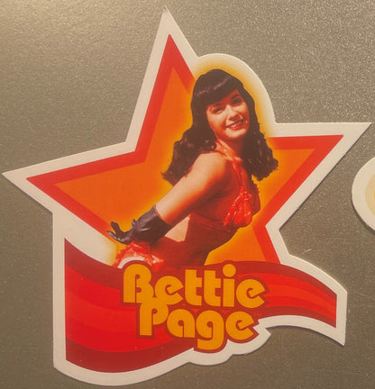 Star-shaped sticker featuring vintage pin-up woman in red outfit with dark hair, orange and red gradient background, "Bettie 