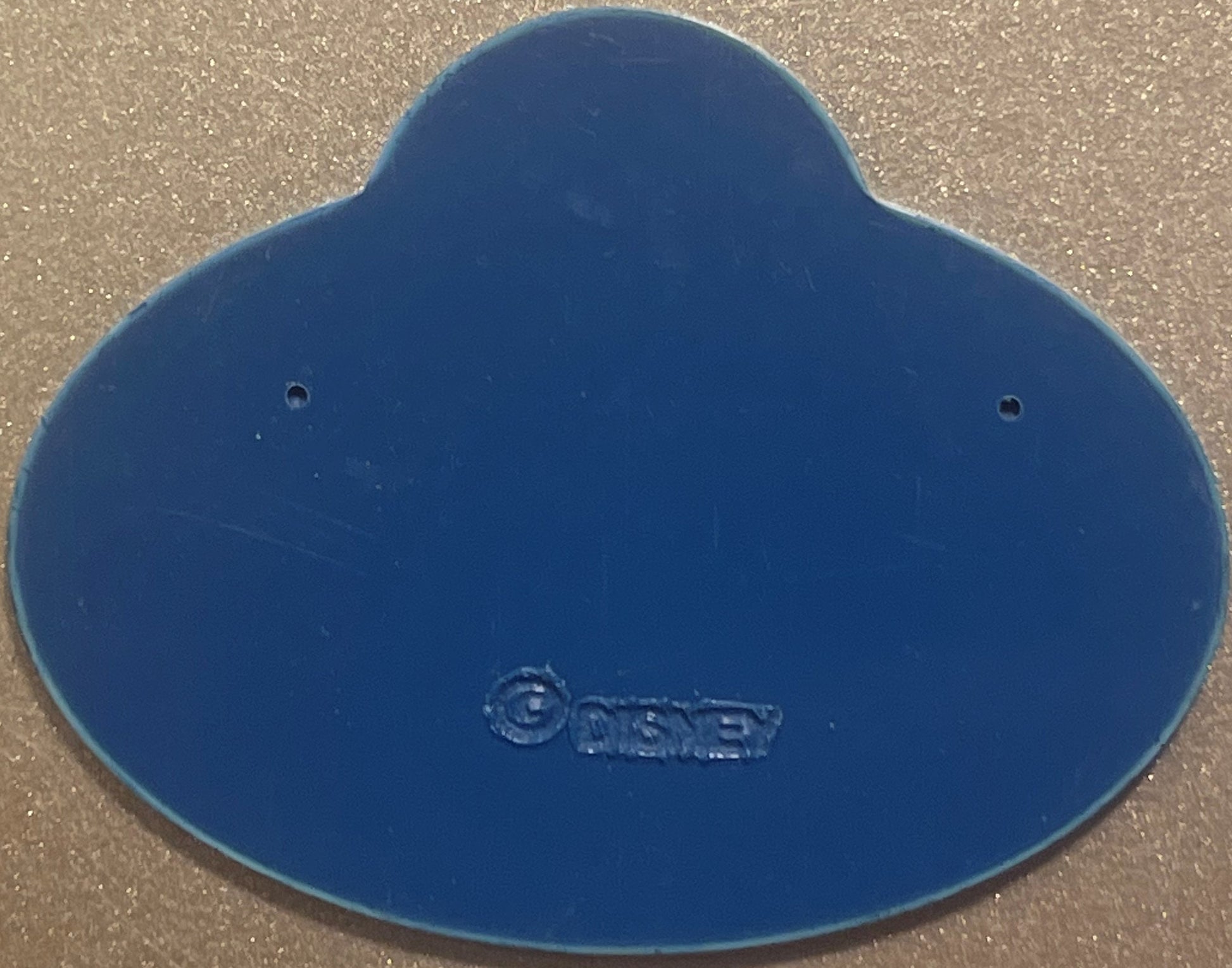 Blue Disney cast member badge with embossed logo, two mounting holes visible, photographed flat on textured surface